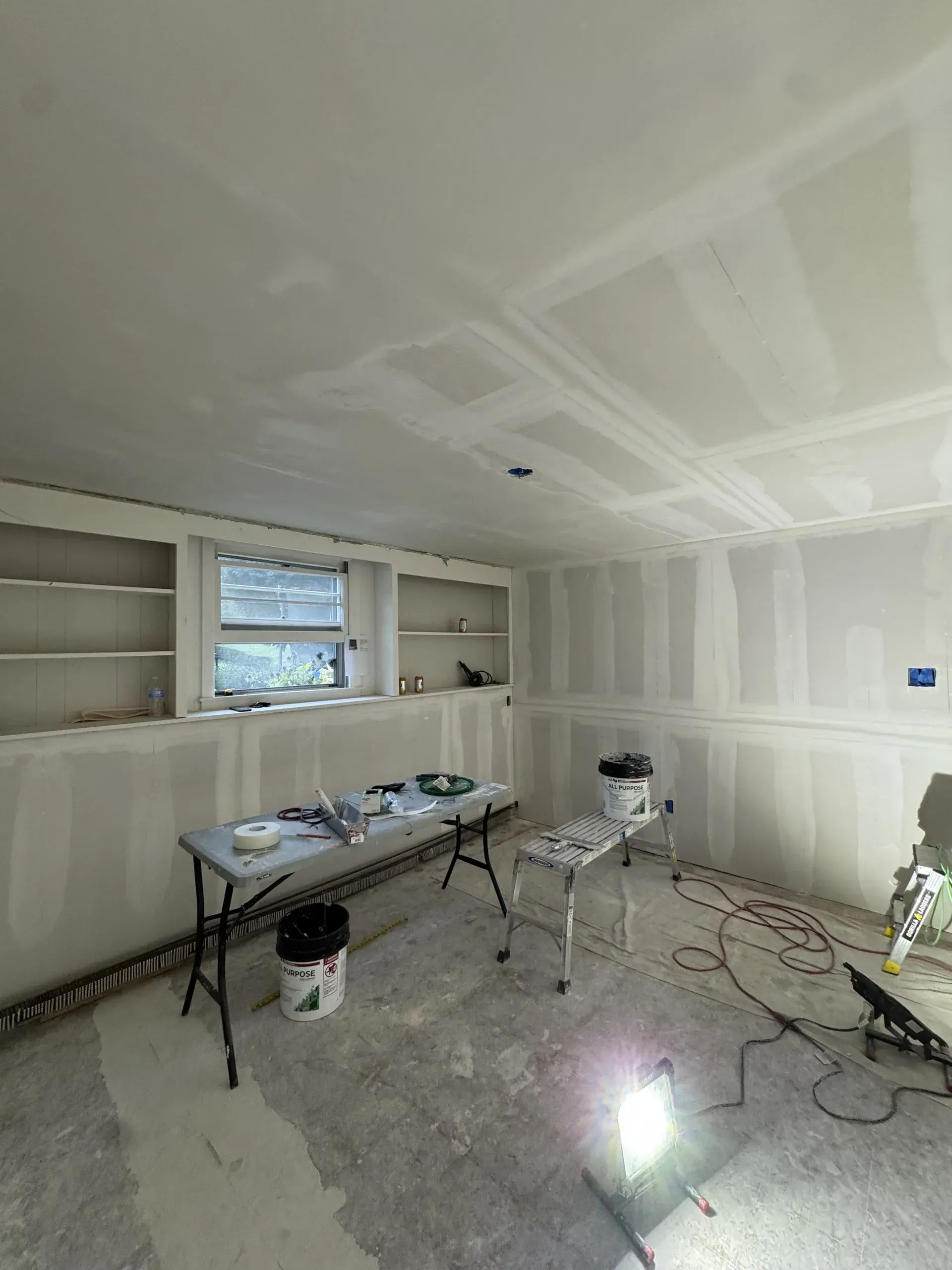 Partially finished room with drywall, tools, and paint supplies on a worktable