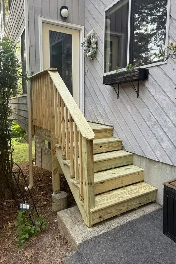 Wooden steps and railing leading to a side entry door on a house with diagonal gray siding