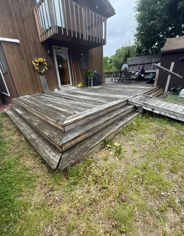 Weathered wooden deck steps beside a house, with a small ramp and backyard grass.