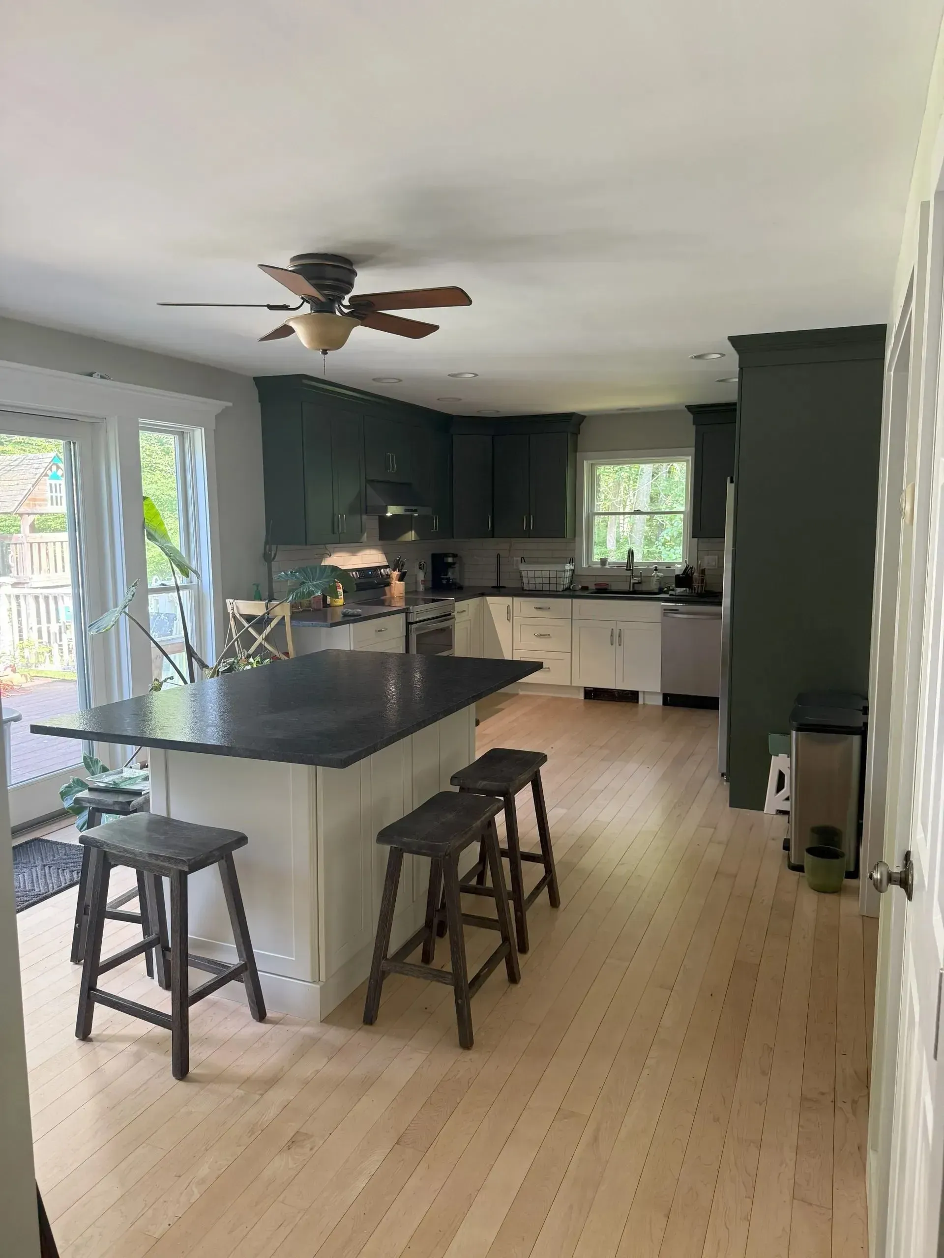 Modern kitchen with dark cabinets, black island, stools, and ceiling fan in an open room