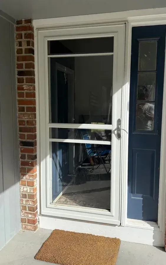 Front porch with a white screen door, brick wall, blue siding, and a tan doormat.