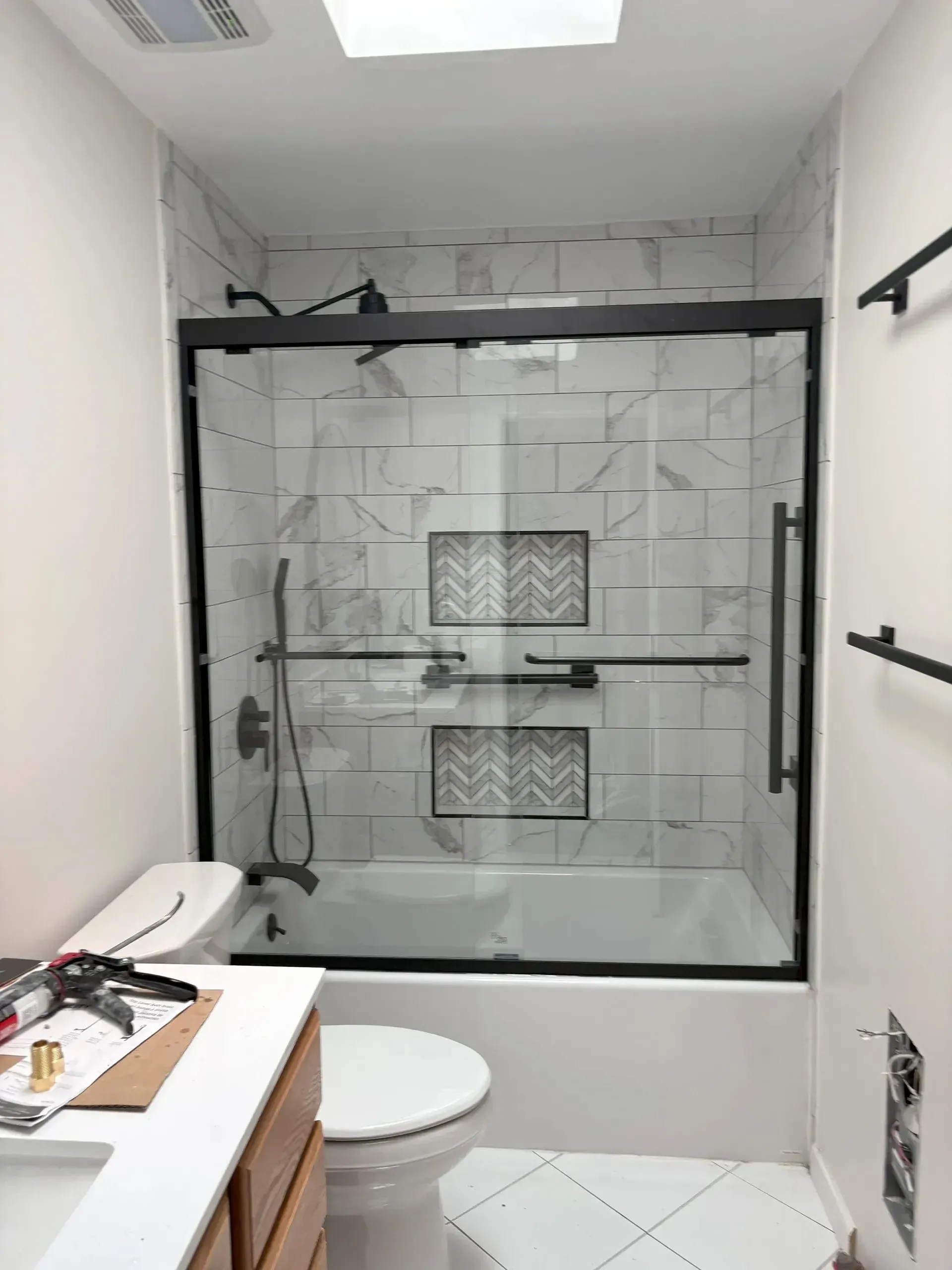 Bathroom with a glass-enclosed shower, toilet, and vanity under a skylight.