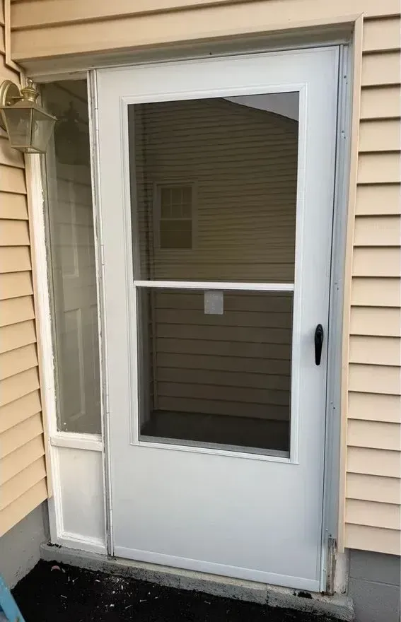 White screen door with a storm window on a beige-sided house exterior.