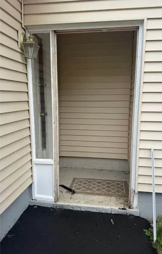 Open doorway with a small step into a beige-sided house, showing a mat inside and a dark porch outside