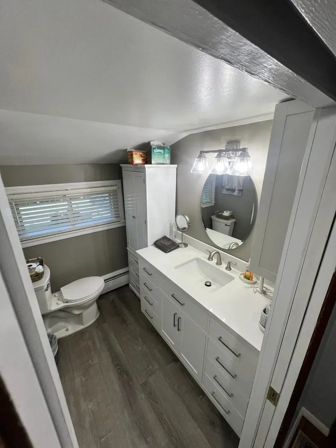 Small bathroom with toilet, vanity sink, mirror, and dark wood floor beneath a sloped ceiling.