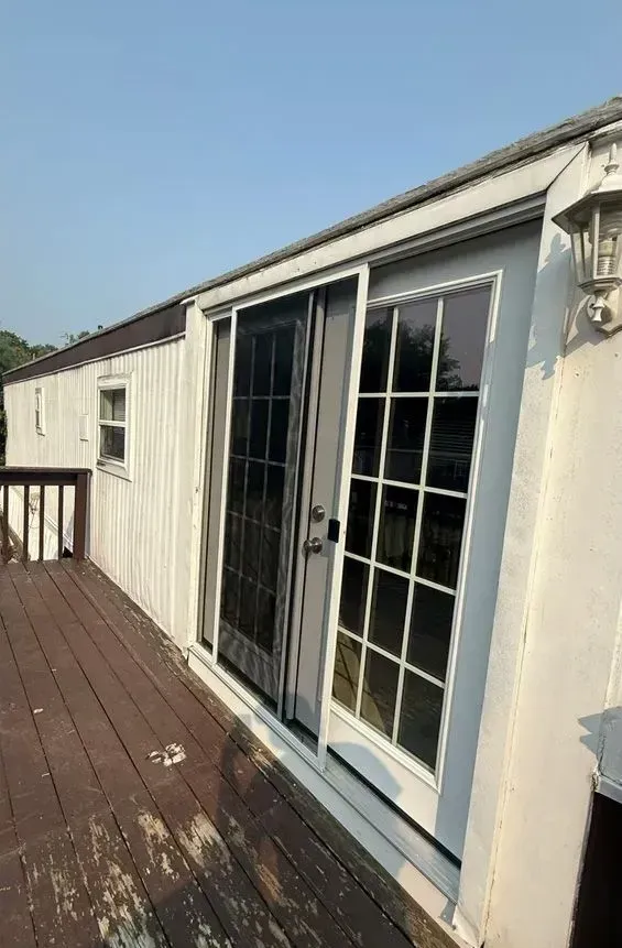 White double French doors on a gray mobile home, opening onto a wooden deck outdoors.