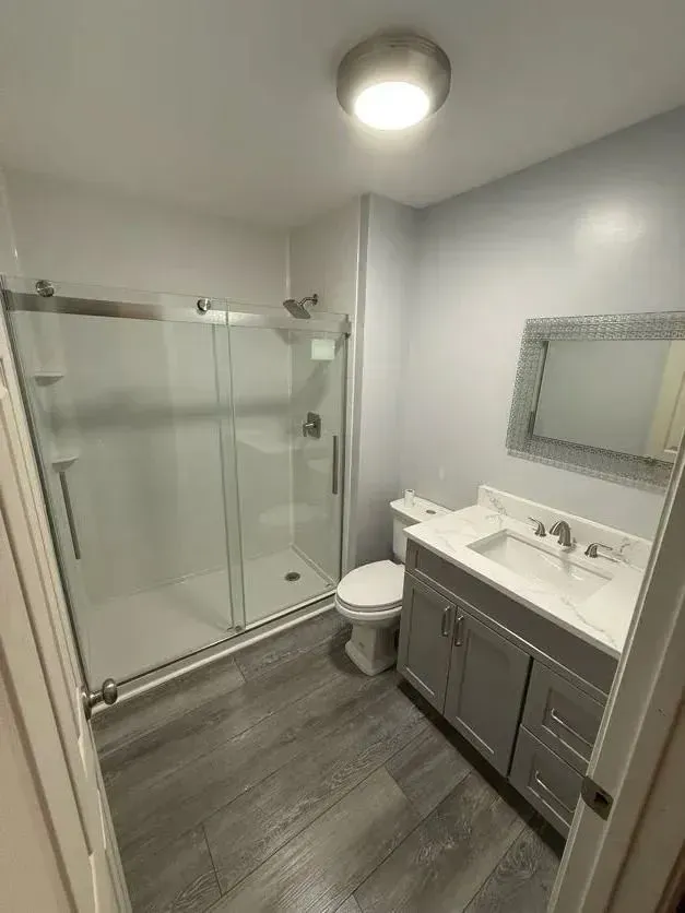 Modern bathroom with glass shower, vanity, toilet, and gray tile flooring