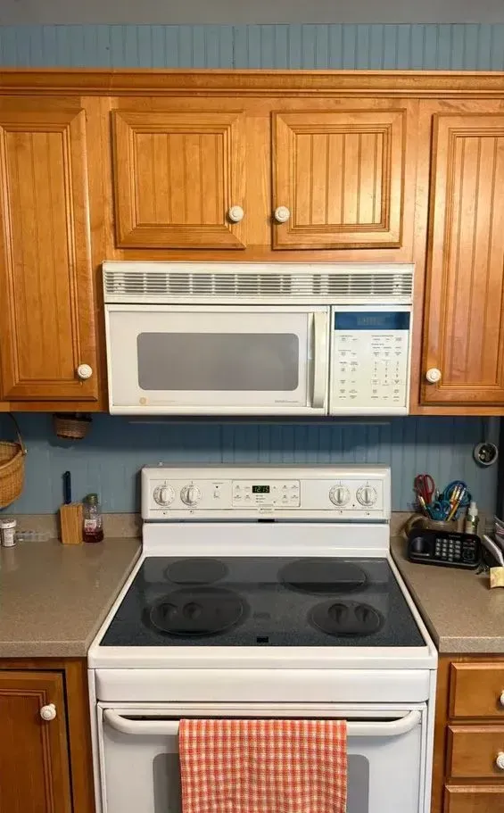 Kitchen with wooden cabinets, white stove and microwave, and blue backsplash.