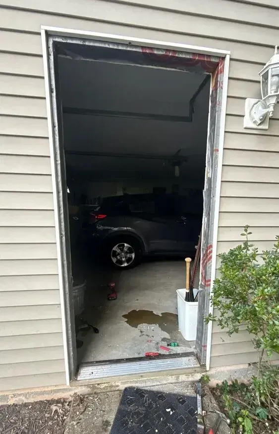 Open doorway to a dim garage with a parked dark car and some items by the threshold