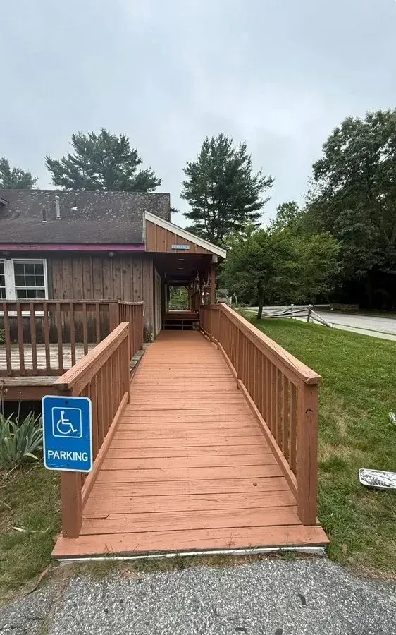 Accessible wooden ramp leading to a building entrance, with blue handicap parking sign nearby.