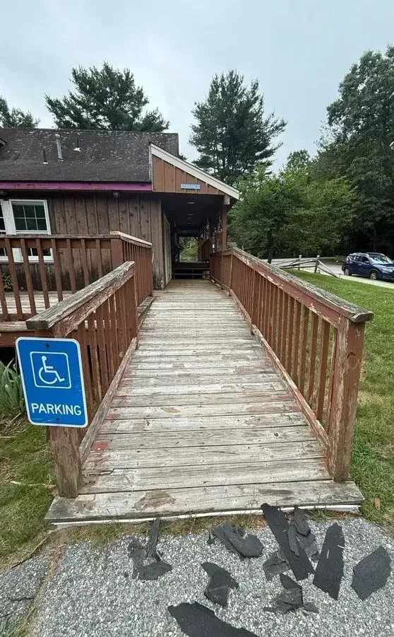 Accessible ramp to building entrance with blue handicap parking sign and wooden railings.
