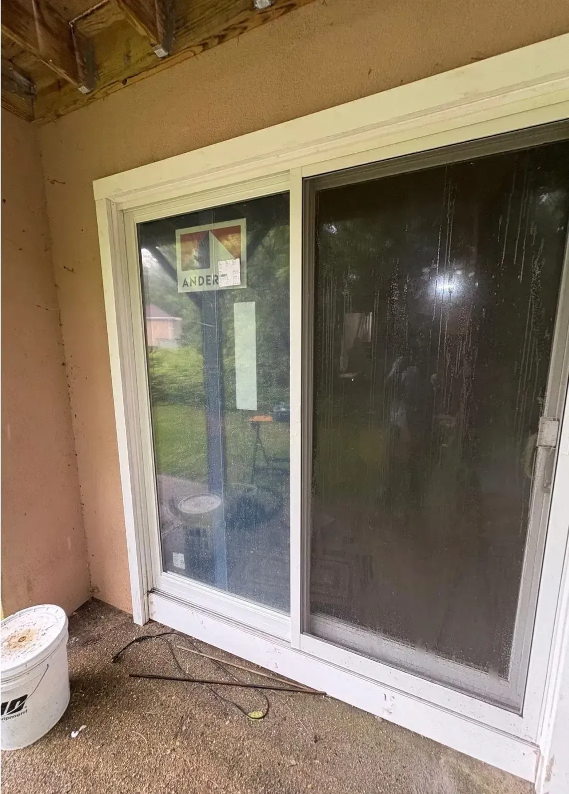 Sliding glass door with white frame on a covered patio, showing a screened side panel and wet concrete floor