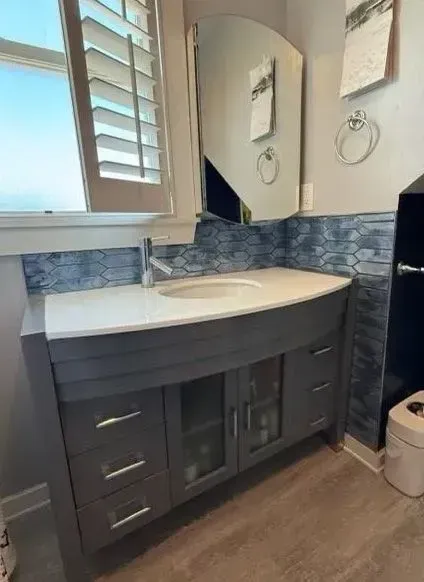 Bathroom vanity with white countertop, dark cabinets, round sink, mirror, and blue tile backsplash