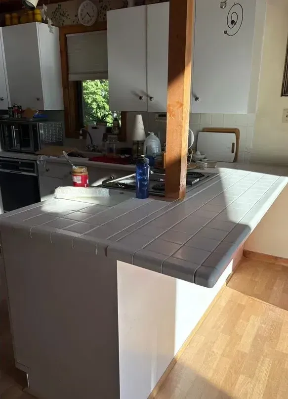 Kitchen island with dark countertop, white cabinets, and a wooden support beam in a bright home interior