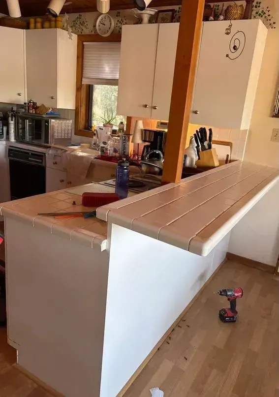 Kitchen under renovation with white cabinets, unfinished island counter, and tools on the floor