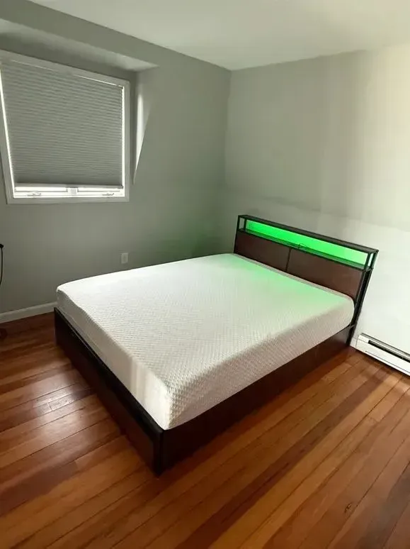 Empty bedroom with a bed, hardwood floors, gray walls, and a window with blinds.