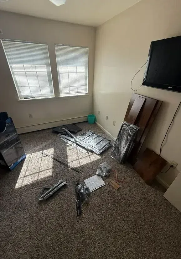 Messy carpeted room with broken TV parts and debris beneath a wall-mounted television