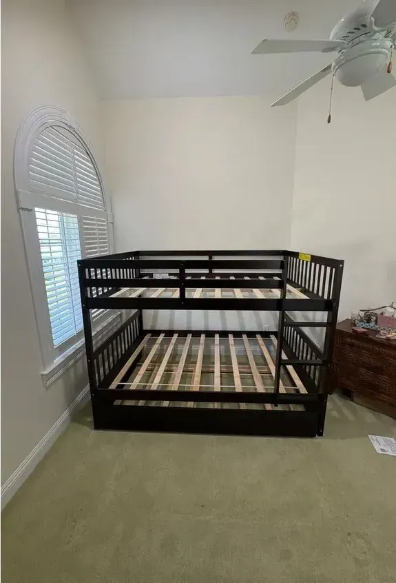 Black bunk bed in a beige bedroom with a window and ceiling fan