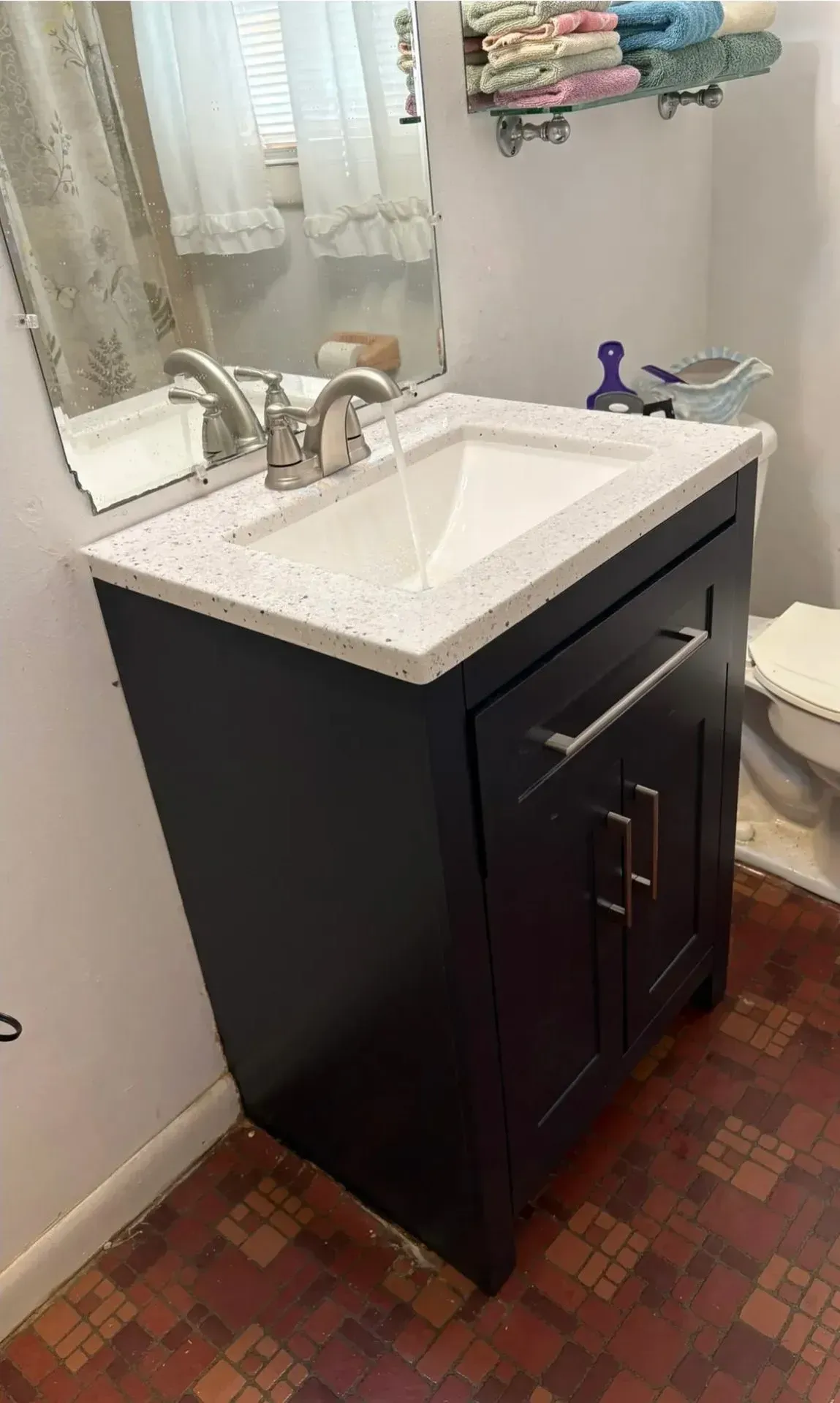 Bathroom vanity with white sink top, dark cabinet, mirror, and towel rack on a tiled floor.