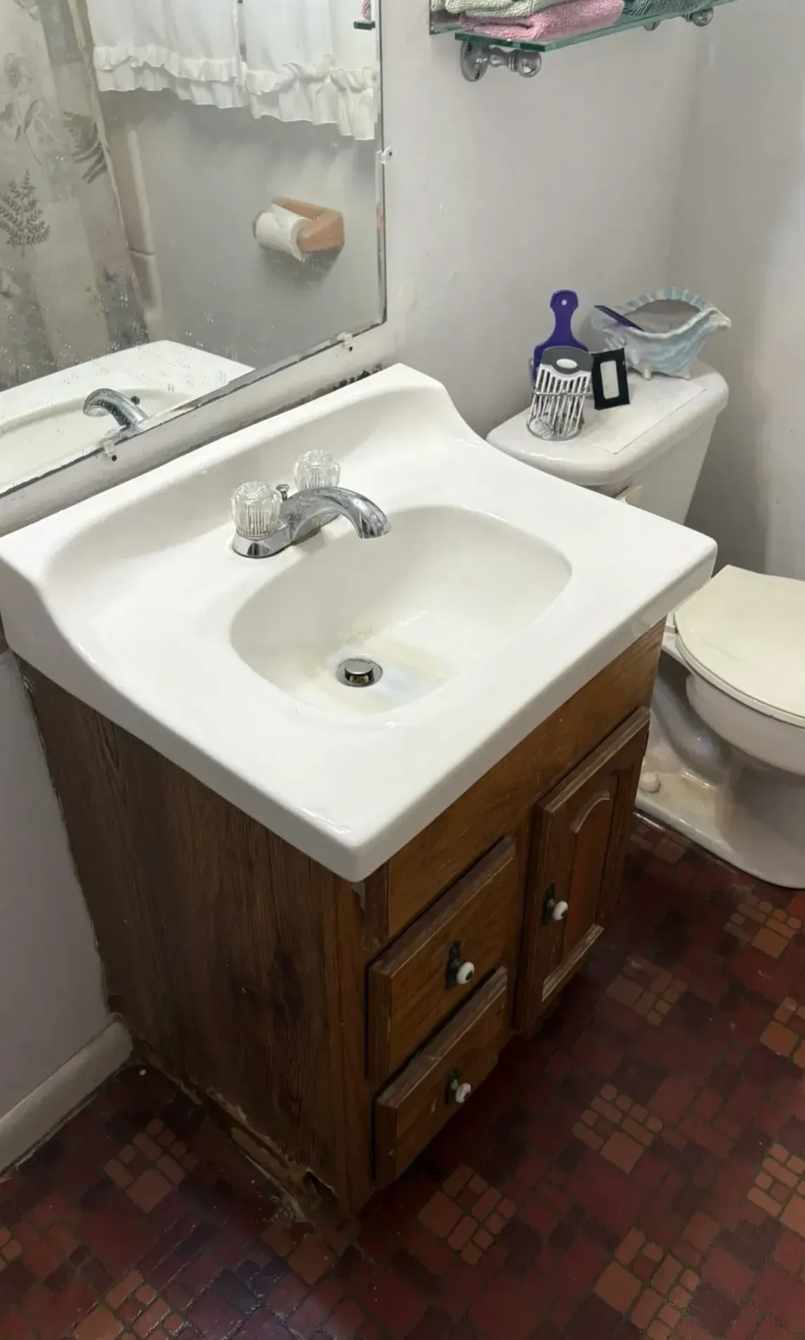 Small bathroom with white sink, wooden vanity, toilet, and toiletries on the back tank.