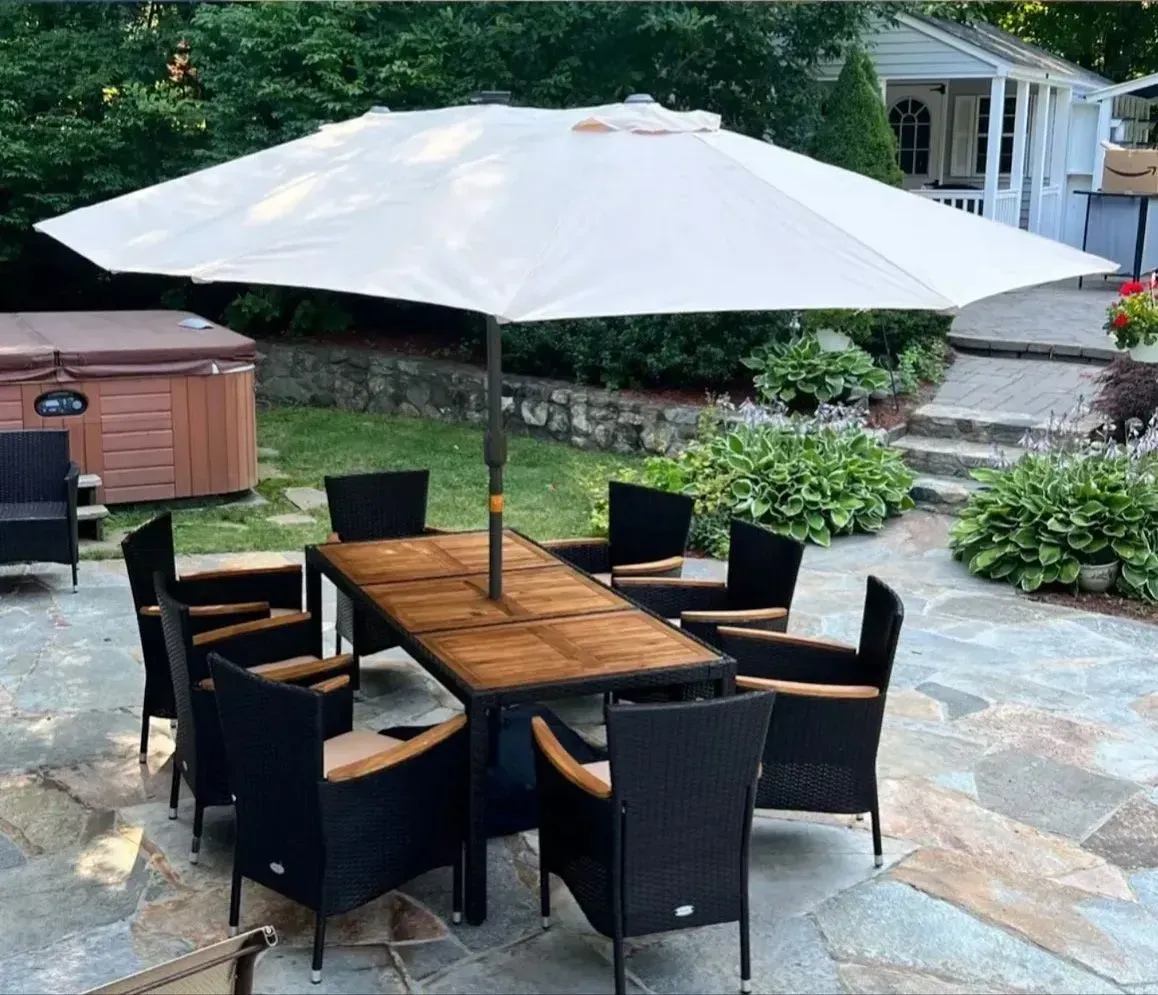 Outdoor patio dining set with wooden table, black chairs, and large white umbrella on stone paving