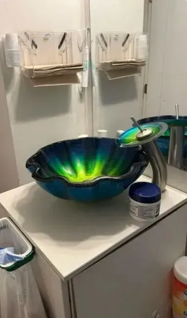 Bathroom vanity with a colorful blue-green sink, mirror, and toiletries on the counter