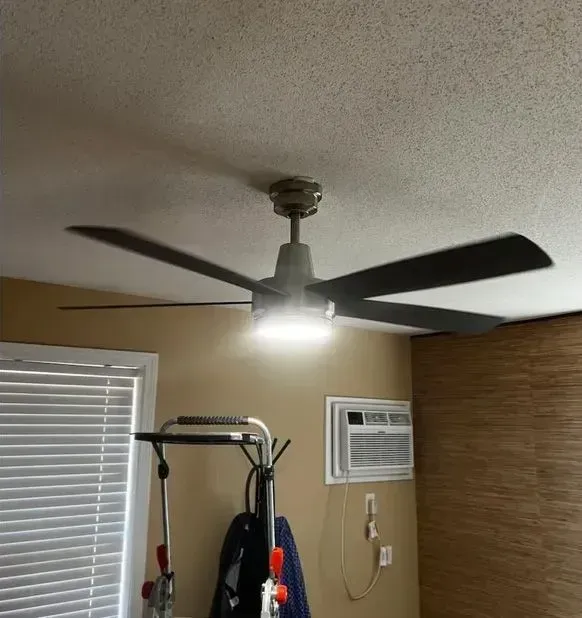 Ceiling fan with light in a small room, above exercise equipment and a wall air conditioner.