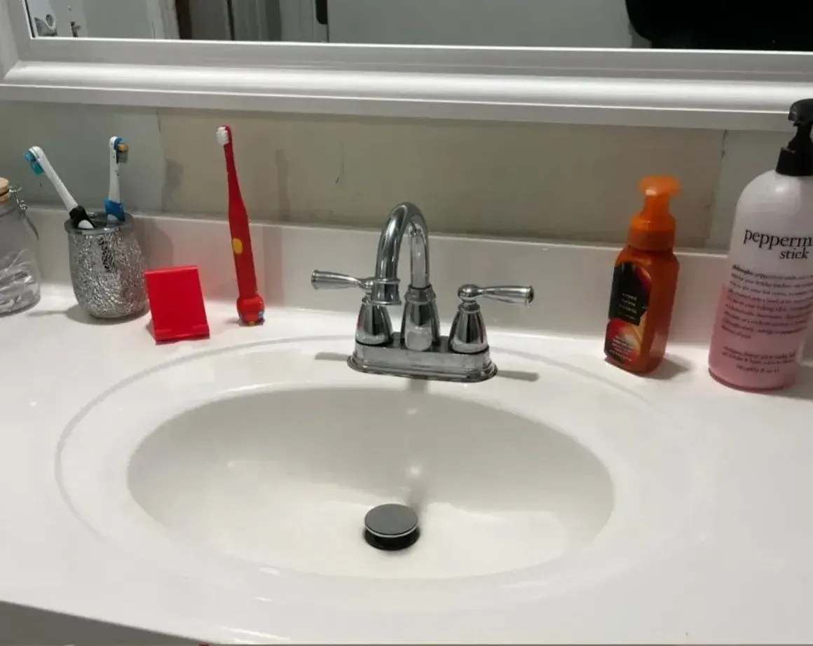 Bathroom sink with chrome faucet and toiletries on the counter, including a red toothbrush and orange soap dispenser