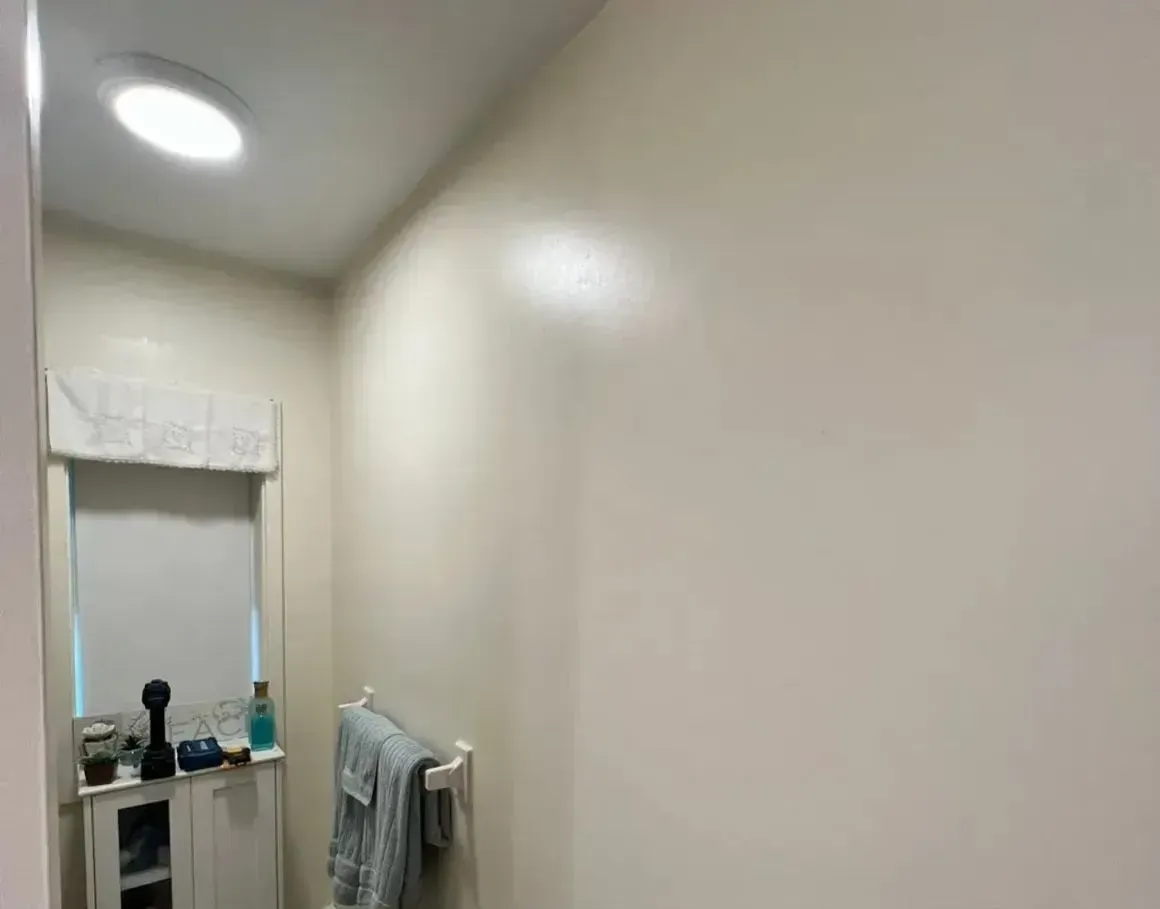 Narrow beige hallway with a small sink, mirror, and towels at the end.