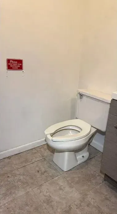Small restroom with a toilet beside a wall-mounted grab bar and a red sign on the wall.