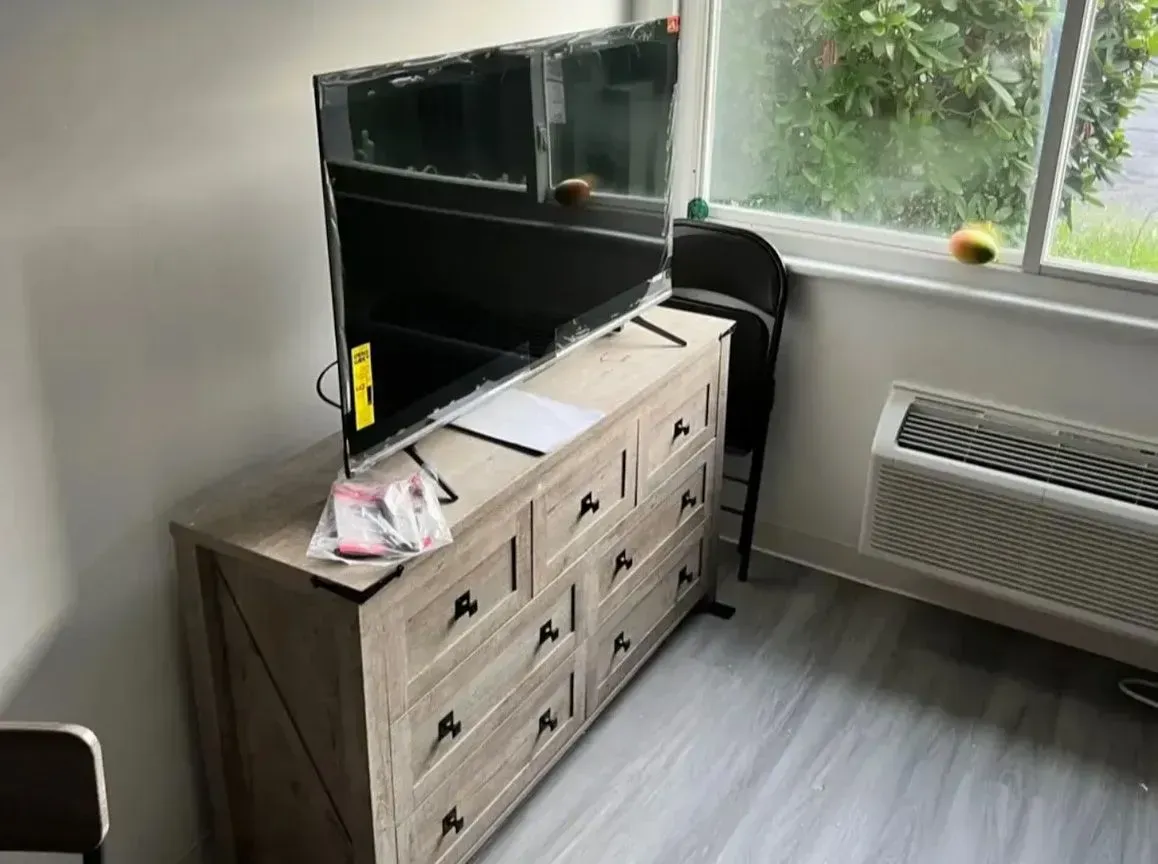 Living room with TV on a dresser, chair, window, and air conditioner over gray flooring