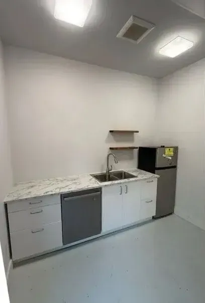 Small kitchenette with white cabinets, marble-look counter, sink, stove, and black refrigerator under bright ceiling lights