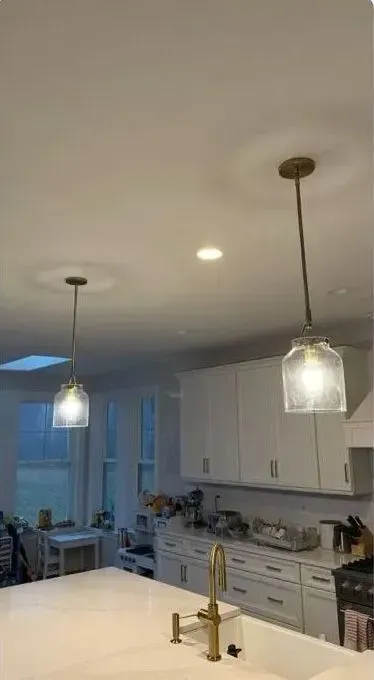 Modern white kitchen with pendant lights, island, cabinets, and large windows.