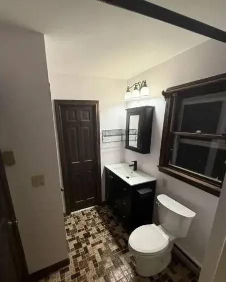 Small bathroom with patterned tile floor, black vanity, white toilet, wall mirror, and window.