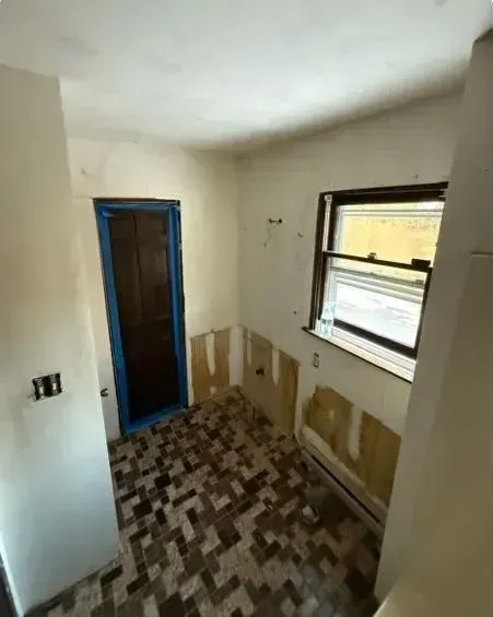 Small unfinished bathroom with tiled floor, window, blue-trimmed doorway, and exposed wall patches