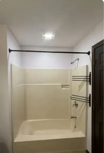 Accessible bathroom with a beige bathtub, grab bars, shower rod, and towel rack behind a curtainless shower.