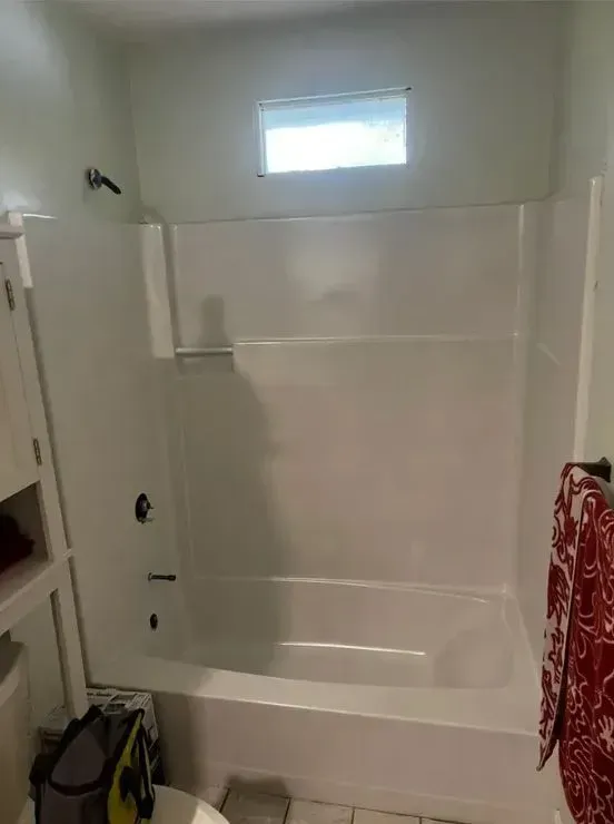 White bathtub and shower with frosted window, grab bar, and red towel in a small bathroom