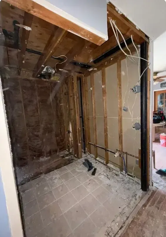 Partially demolished room with exposed wooden studs, ceiling beams, and tiled floor under renovation