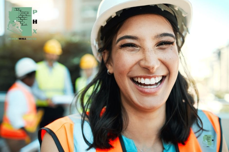 Block wall repair specialists work on a commercial project, with a smiling female worker in an orange safety vest and hard hat in the foreground near N Toledo Ave, and W Santa Clara Ave in Maricopa, AZ.