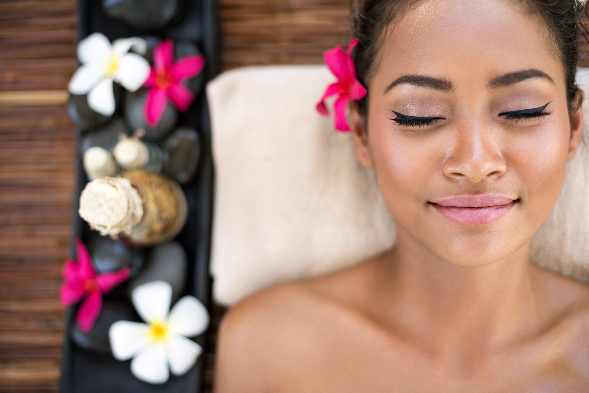 A woman is laying on a massage table with her eyes closed and flowers in her hair.