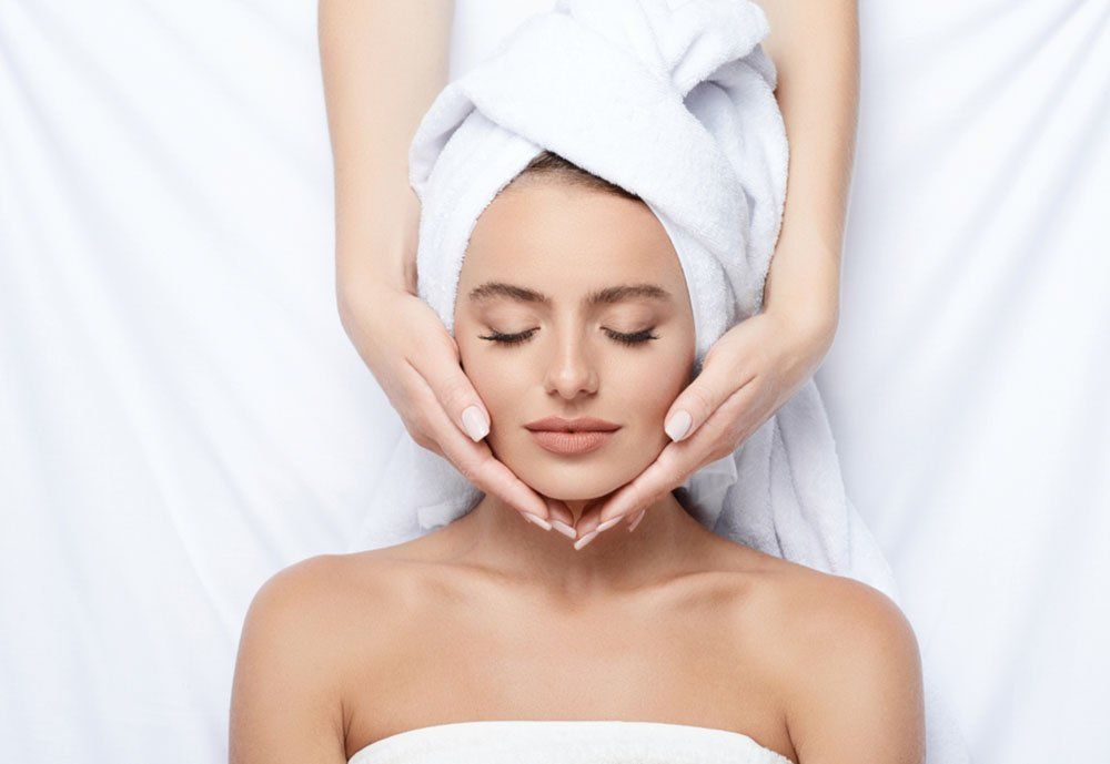 A woman with a towel wrapped around her head is getting a facial massage.