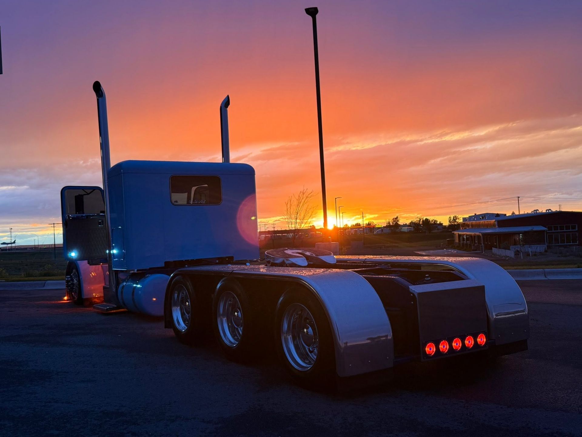Blue semi truck at sunset with glowing red taillights in a parking lot