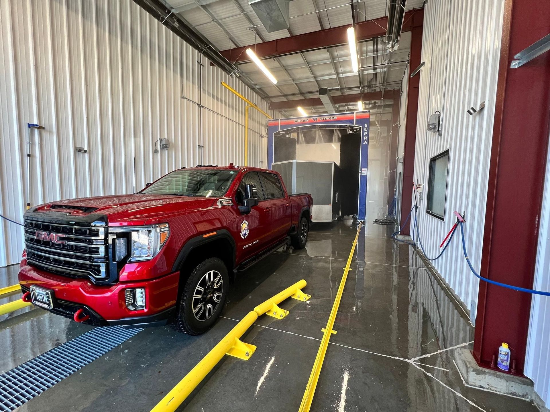 Red pickup truck in a service bay with corrugated metal walls and bright yellow floor rails.