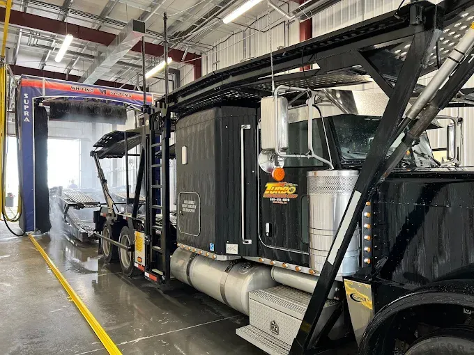Black semi-truck in an indoor wash bay with a yellow hose and wet floor