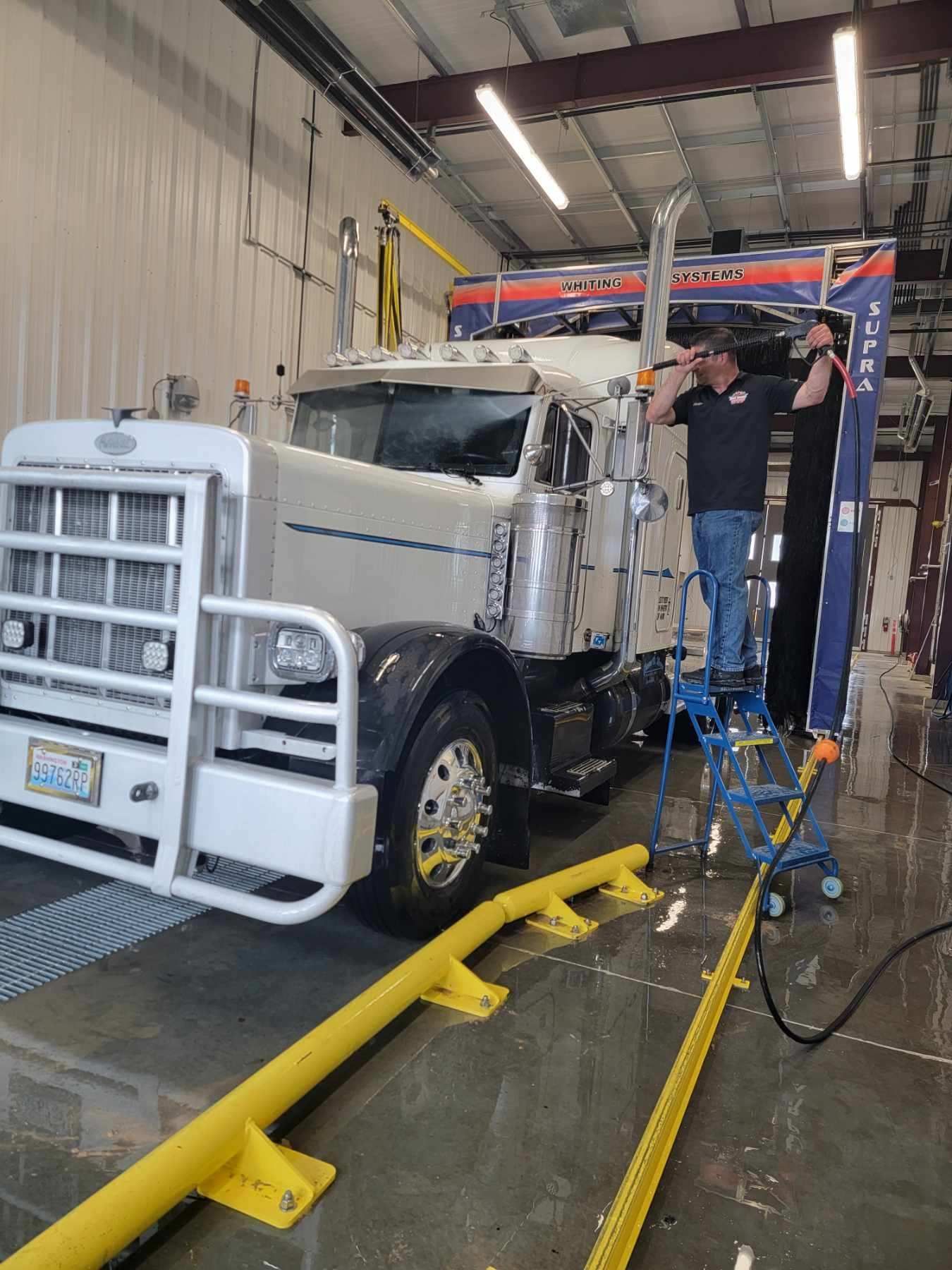Truck being washed in an auto bay, with workers using a pressure washer and drying tools