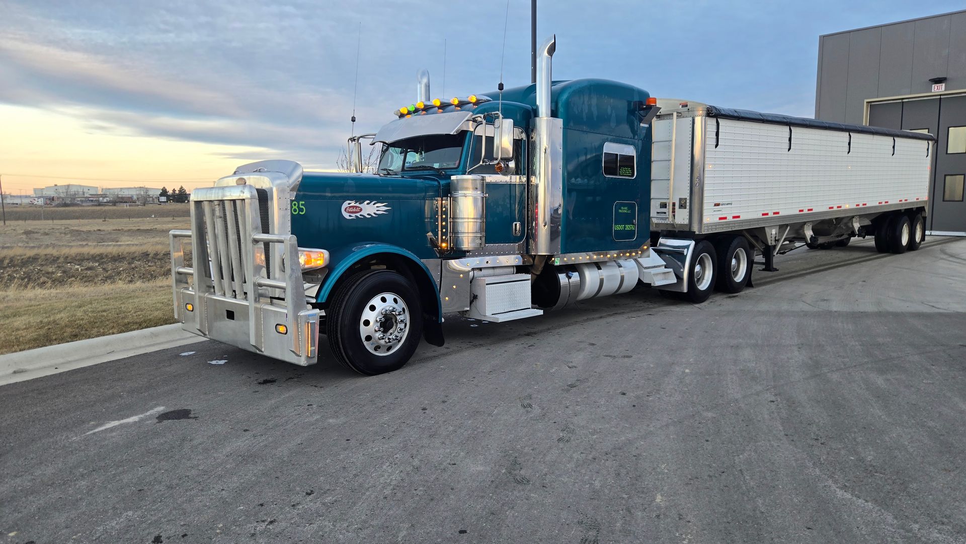 Blue semi truck with white trailer parked on a roadside at sunset.