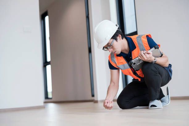 An Asian worker in safety gear performing floor inspection inside a building with clipboard in hand