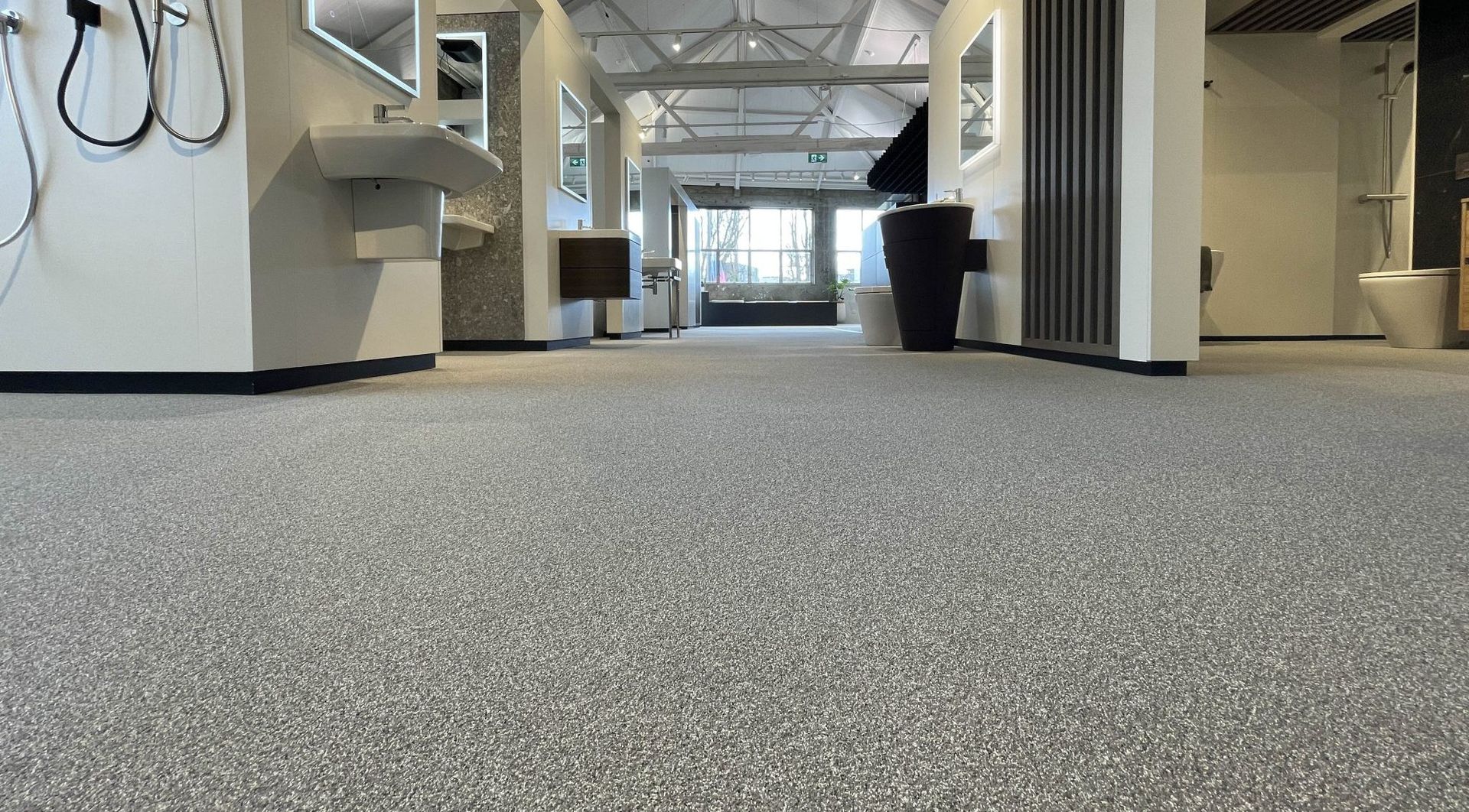 Low-angle view of a showroom floor with speckled gray surface, various bathroom fixtures in the background.