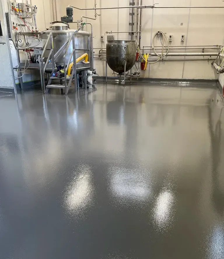 Factory floor with shiny, gray epoxy coating and industrial equipment.