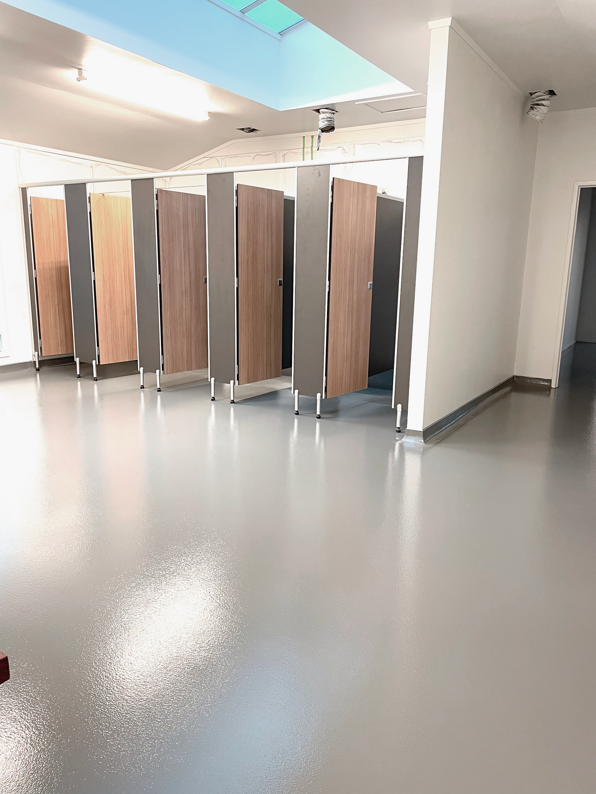Public restroom with multiple stalls, shiny gray floor, and natural wood doors.